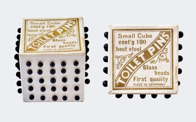 white cube filled with straight pins (black heads)
