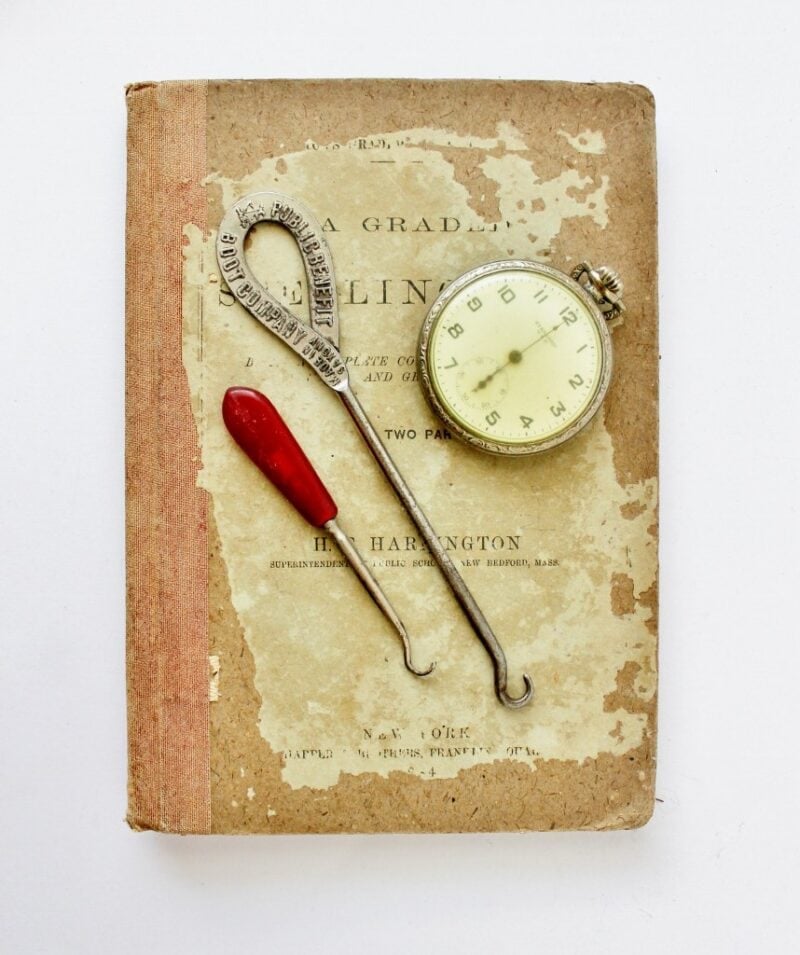 Pair of antique button hooks on an antique book next to an antique pocket watch