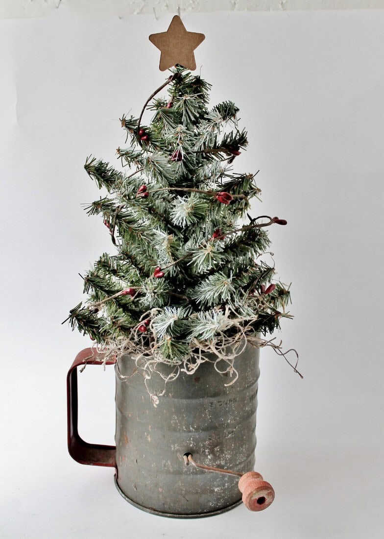 a christmas tree in an antique flour sifter