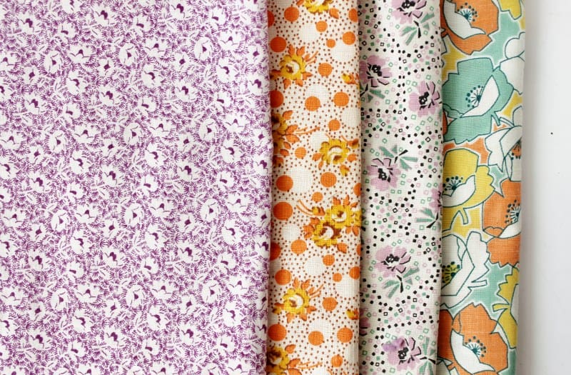 Four pieces of vintage feedsack fabric in lavender, orange and multi-colors