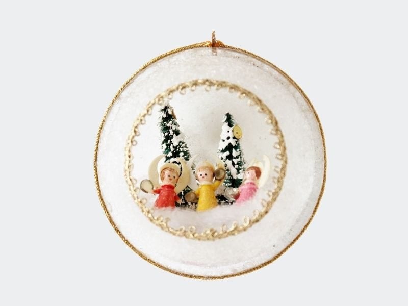 round white plastic ornament with trees and angels inside opening